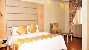 Une chambre d’hôtel avec un grand lit, une chaise, une petite table et une fenêtre avec des rideaux.