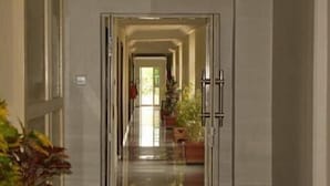 Un couloir doté d’un sol réfléchissant mène à une porte munie d’une poignée en métal. Des plantes en pot sont disposées le long du couloir.