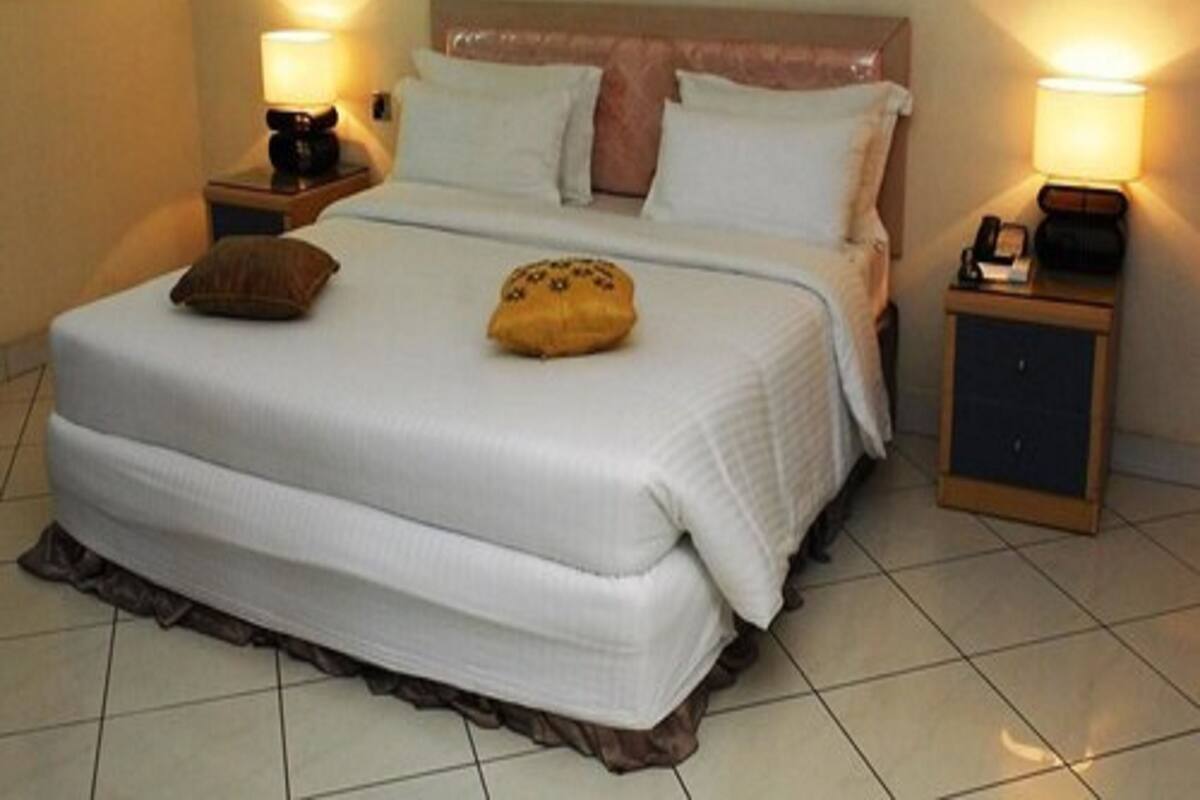 A neatly made bed with a white duvet, two pillows, and a decorative pillow on the headboard. There are two bedside tables with lamps, one on each side of the bed.