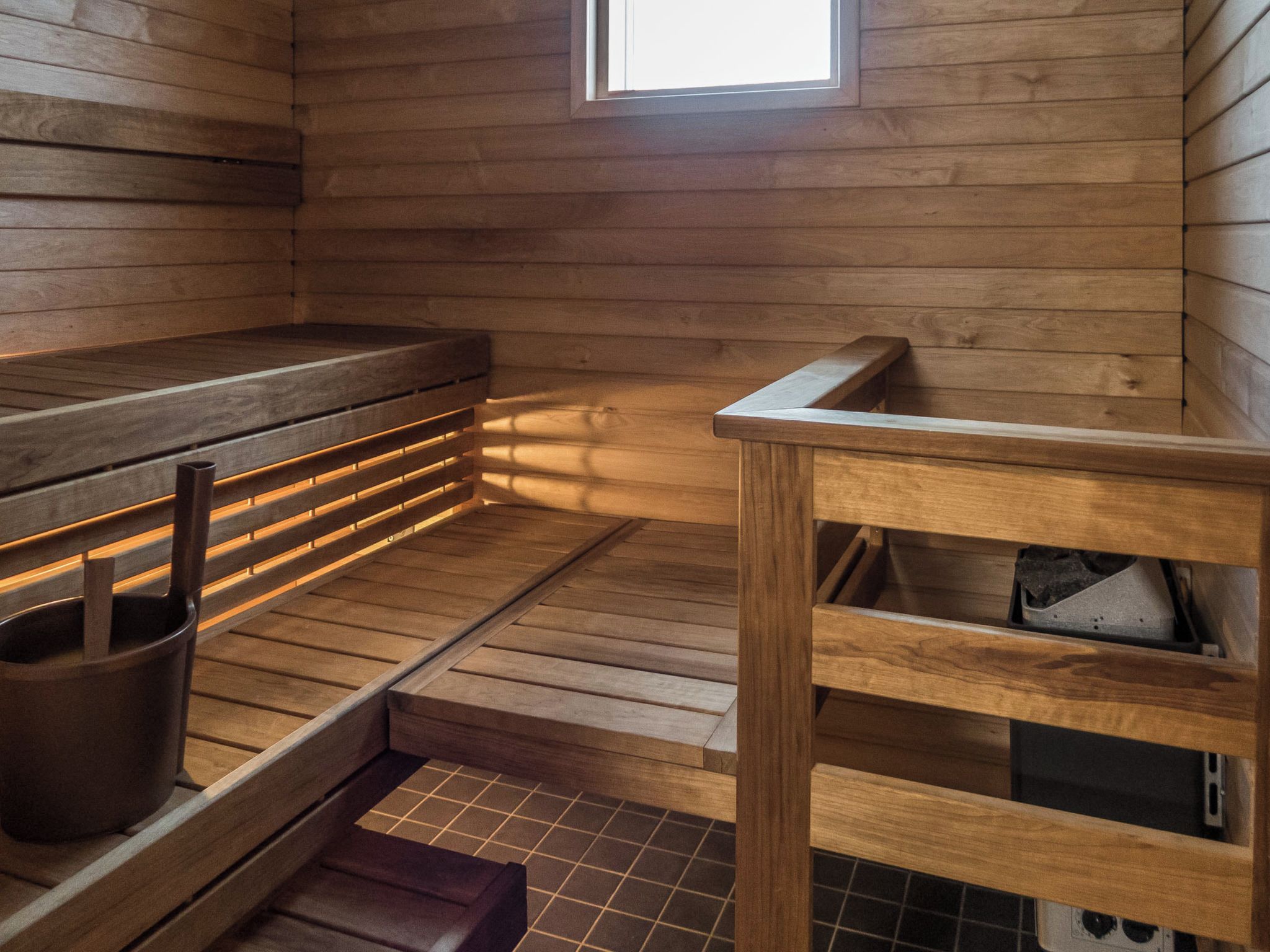 Una sala de sauna con bancos de madera, un ventanal pequeño y suelo de baldosas.