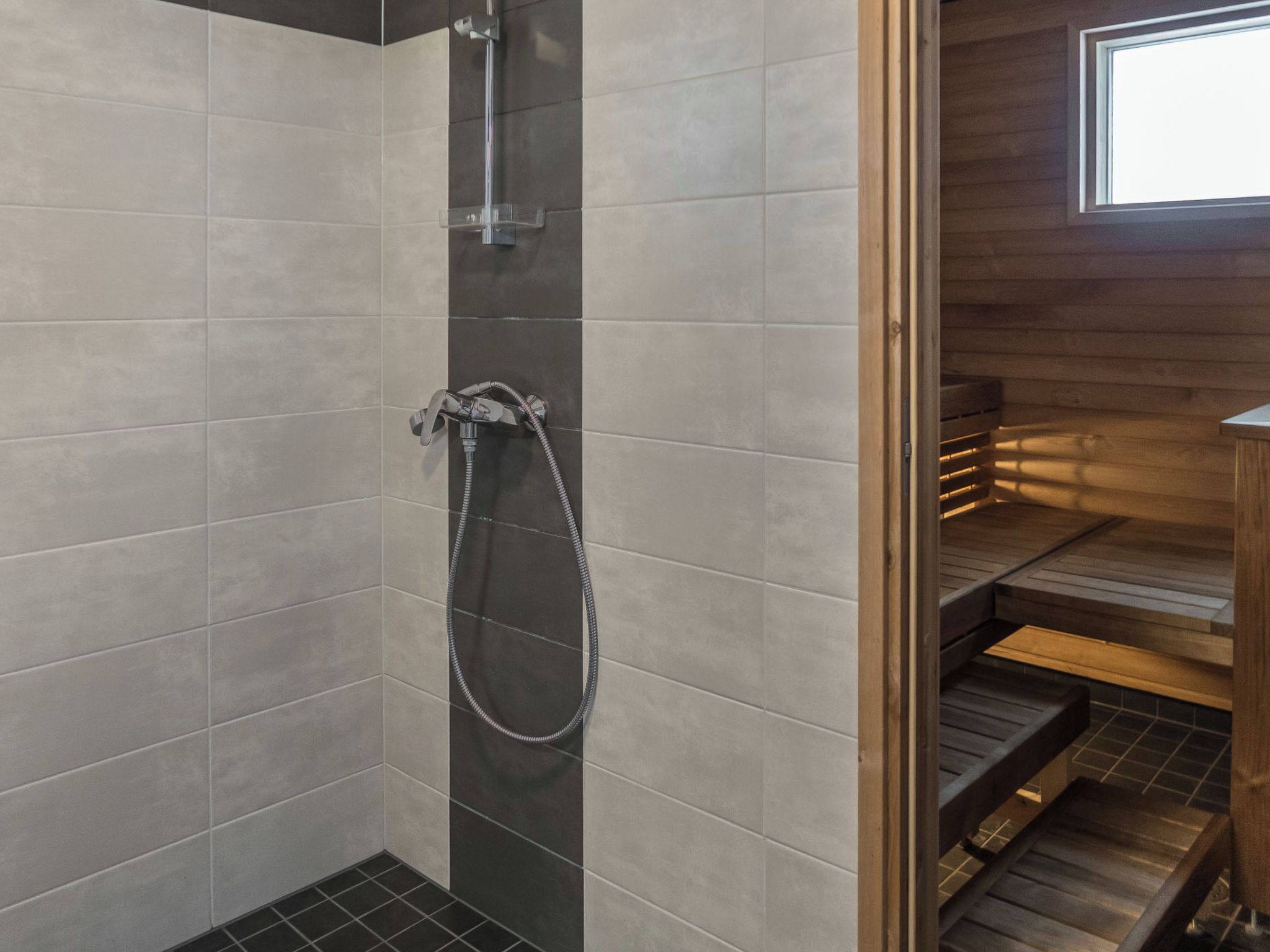 Un espace douche doté d’une porte en verre, de murs carrelés et d’un banc en bois.