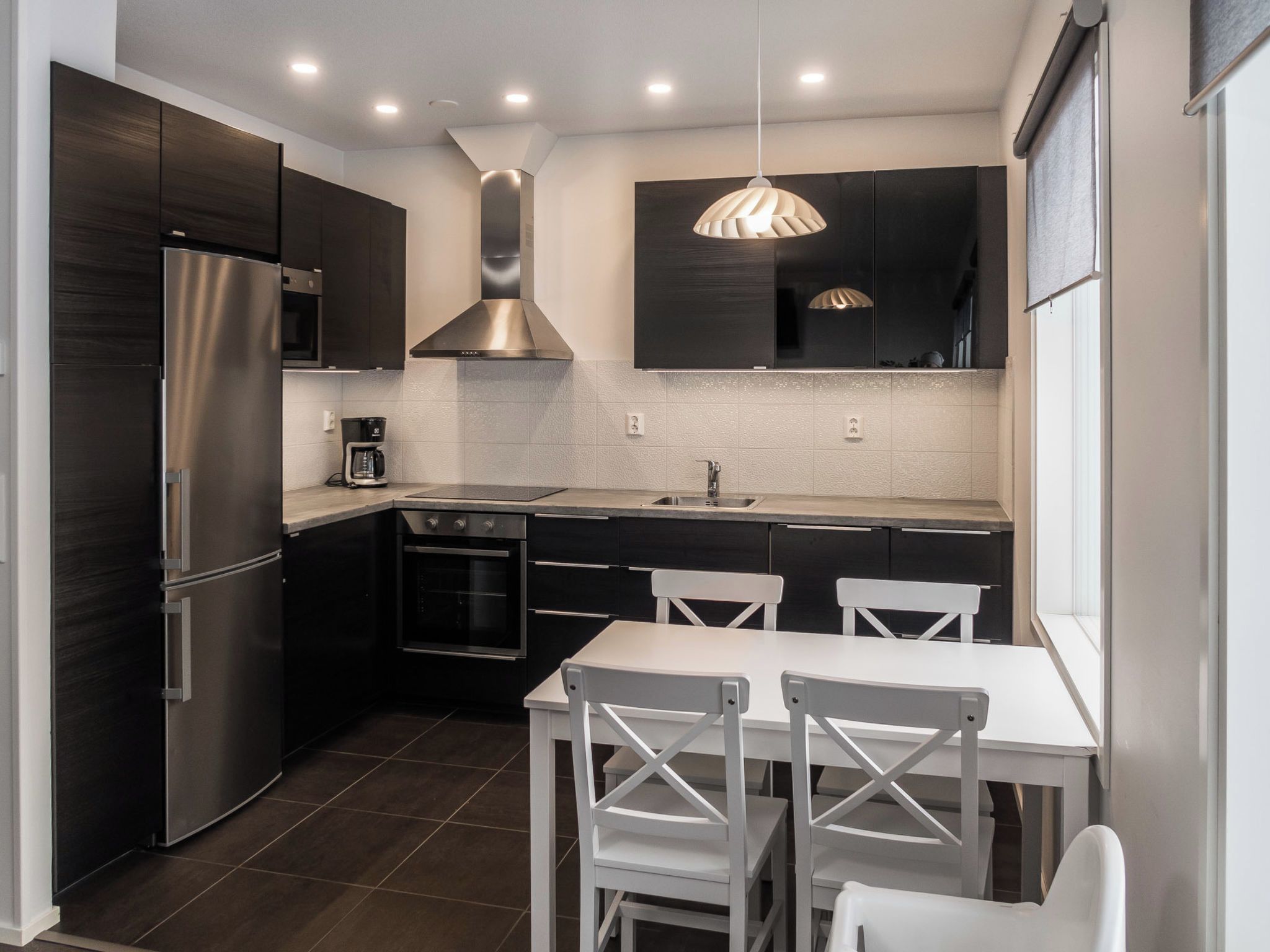 A modern kitchen with dark cabinetry, stainless steel appliances, a white dining table, and pendant lighting.
