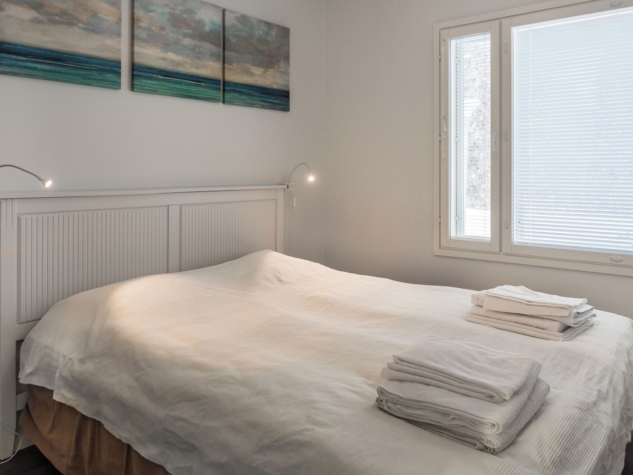 Un dormitorio con cama, un radiador, una ventana con persianas y una lámpara fijada a la pared.