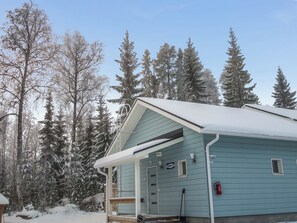 A light blue cabin with a snow-covered roof, surrounded by tall evergreen trees. - Klz rodoniitti by Interhome (Sotkamo)