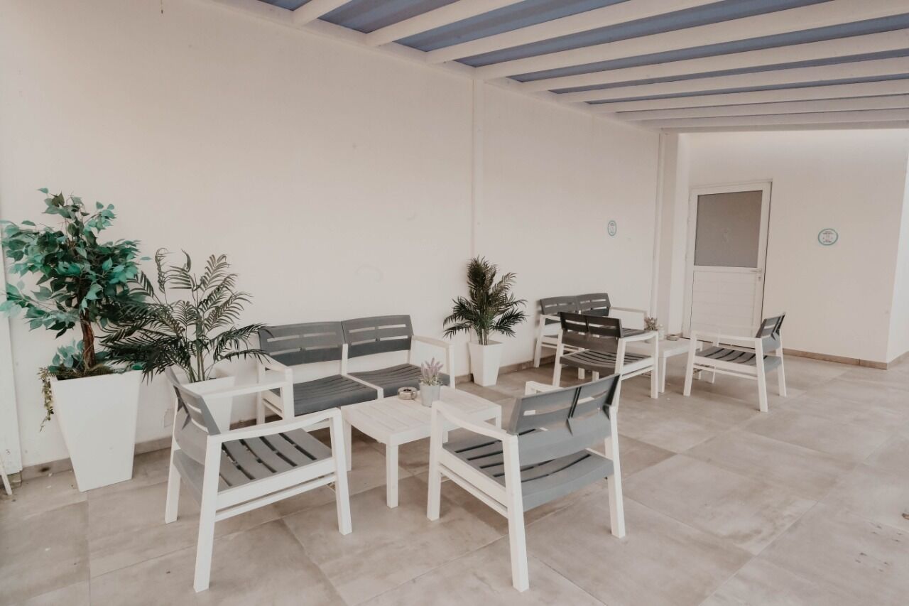 A spacious patio with white furniture, including sofas and tables, surrounded by potted plants.