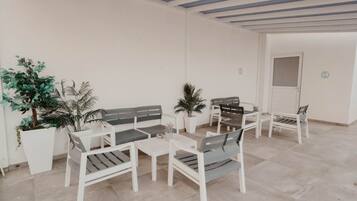 A spacious patio with white furniture, including sofas and tables, surrounded by potted plants.