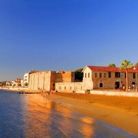 Una zona costera con un muro de piedra, un edificio de techo rojo y una playa.