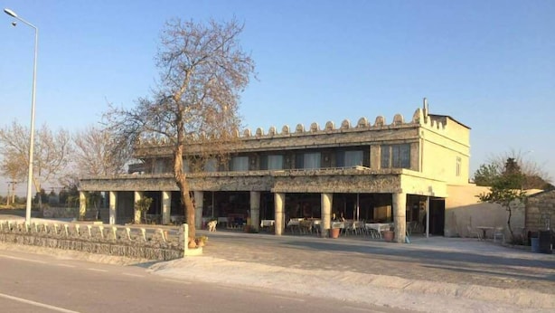 A two-story building with a stone facade and multiple windows. There is a paved area in front with a few potted plants. - Hisarlik Hotel (Çanakkale)