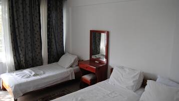 A hotel room with two single beds, a wooden dresser, a mirror, and a window with curtains.
