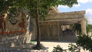 A courtyard with a stone wall, a tree, and a building entrance. - Hisarlik Hotel (Çanakkale)