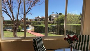 A room with a large window, a striped chair, a round glass table, and a vase with red flowers. - Apartment Las Brisas (Mijas-Costa)