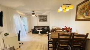 A living room with a sofa, a dining table with chairs, a ceiling fan, and a painting on the wall. - Apartment Las Brisas (Mijas-Costa)