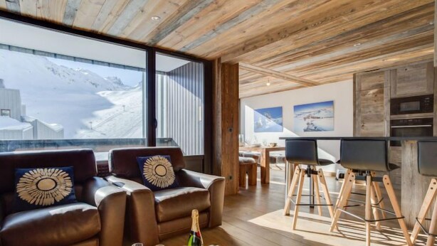Un salon moderne avec des canapés en cuir, un plafond en bois et une grande fenêtre donnant sur un paysage enneigé.
