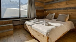 Une chambre avec une grande fenêtre, des murs en bois, un lit avec des oreillers et une vue sur un paysage enneigé.