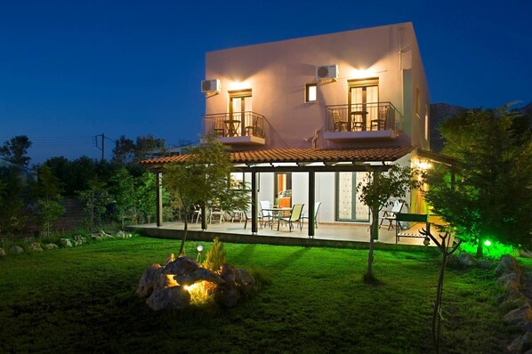 A modern two-story house with a balcony, outdoor seating, and a well-maintained garden.