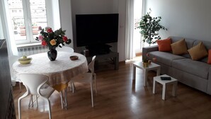 Un salon avec un téléviseur, un canapé, une table à manger avec des chaises et une plante en pot.