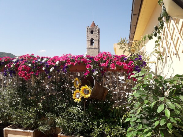 Un jardín con diversas plantas y flores, un pérgola de madera y una torre alta al fondo.