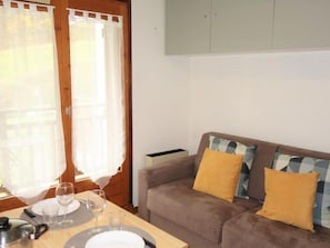 Un coin repas avec une table dressée pour deux personnes, un canapé agrémenté de coussins à motifs et un meuble placé au-dessus du canapé.