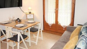 Ein gemütliches Zimmer mit einem Holztisch, vier Stühlen, einem Sofa und einem an der Wand befestigten Fernseher.