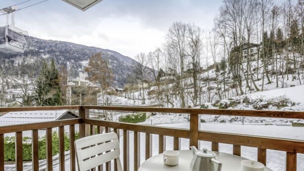 Ein Balkon mit Holzgeländer, einem weißen Stuhl und einem runden Tisch mit Teekanne und zwei Tassen.