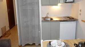 Eine kompakte Küche mit Spüle, Herd und einer kleinen Arbeitsfläche. Ein Esstisch mit einigen Gegenständen ist zu sehen.