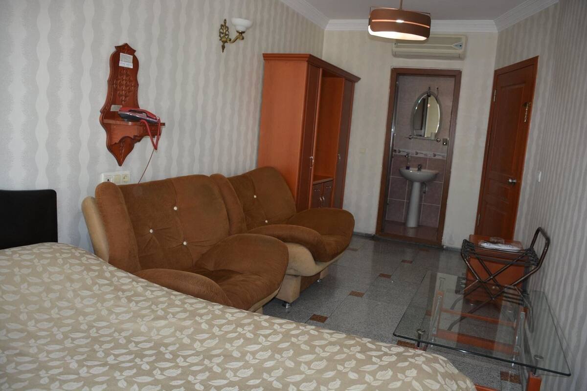 A room with a sofa, a glass table, a wardrobe, and a bathroom with a sink and mirror.