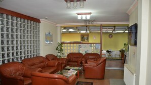 A living room with brown leather sofas, a glass coffee table, and a wall with a map and framed pictures. - Sadikoglu Oteli (Artvin)