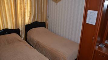 Quarto de hotel com duas camas de solteiro, um guarda-roupa de madeira e uma cortina estampada.