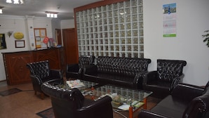 A reception area with a black leather sofa, a glass coffee table, and a wooden reception desk. - Sadikoglu Oteli (Artvin)