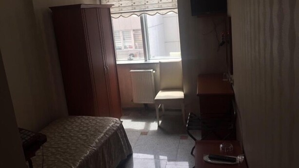 A small, dimly lit room with a bed, a wooden wardrobe, a radiator, a chair, and a television on a stand. - Sadikoglu Oteli (Artvin)