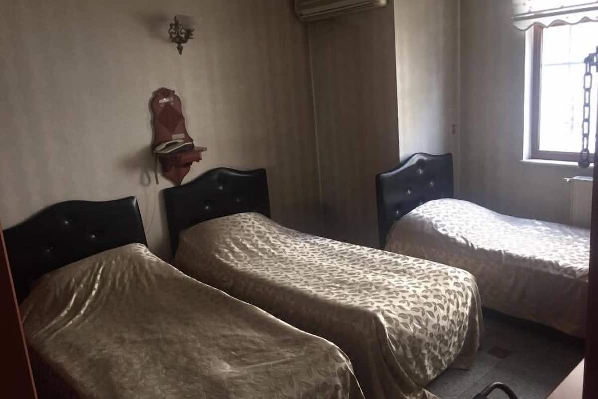 Una habitación con dos camas individuales, un calentador fijado a la pared, una ventana con cortina y una lámpara de pared.