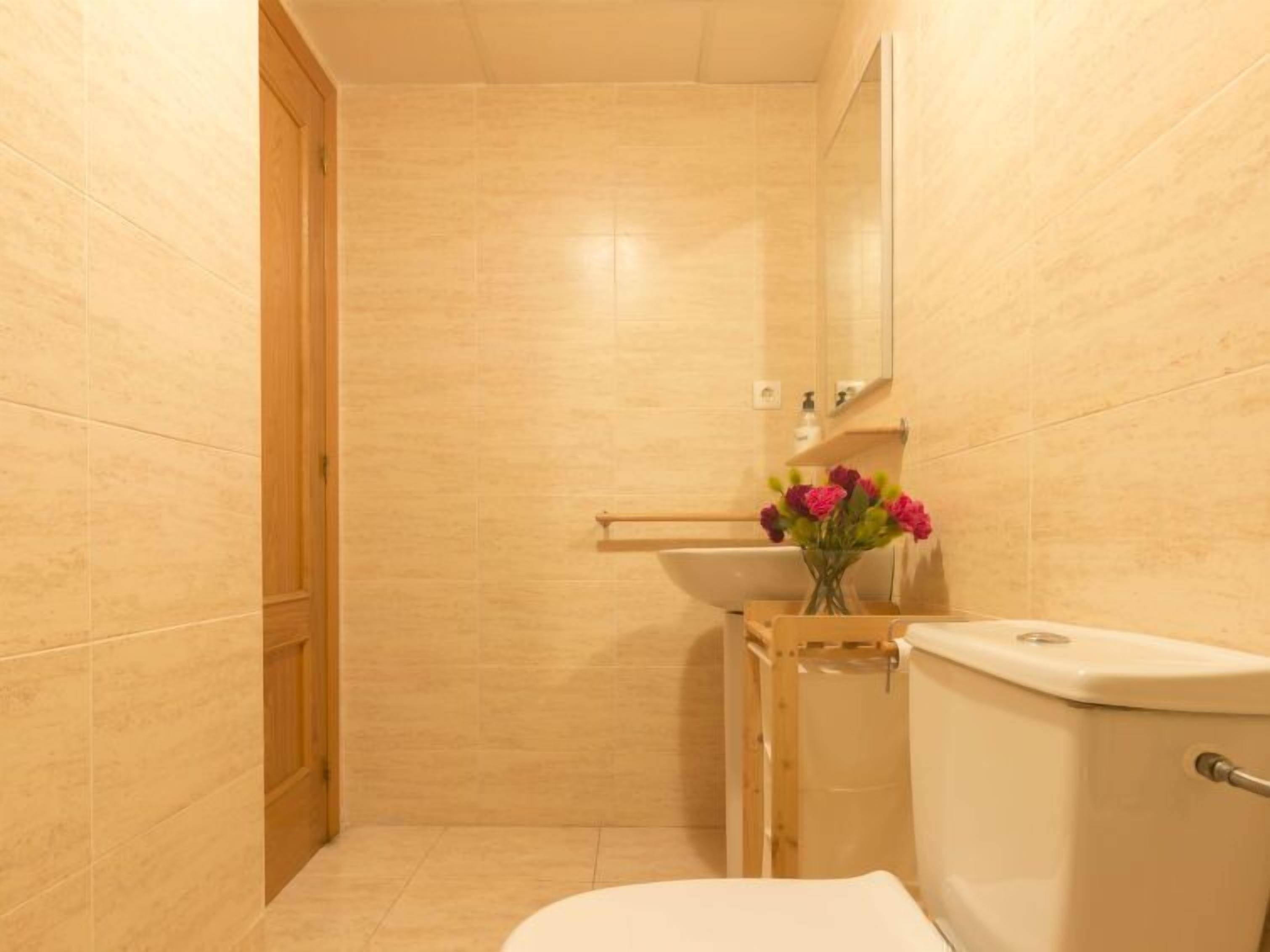 Et badeværelse med beige fliser, et toilet, en vask og et spejl.
