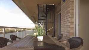 Een balkon met een tafel en stoelen, een plant in een pot en een spiraaltrap.
