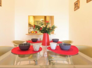Un comedor con una mesa de vidrio, individuales rojos y un jarrón de flores.