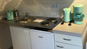A compact kitchen with a stove, sink, and a dishwasher. There are two coffee makers and a kettle on the countertop. - Kleine Möwe (Dornum)