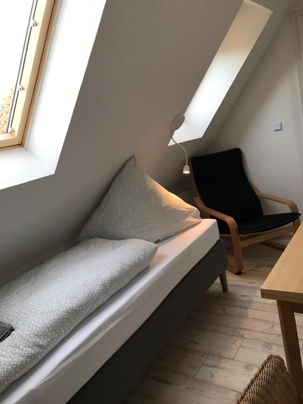Una habitación estilo loft con techo inclinado, un sofá, una silla y una mesa.