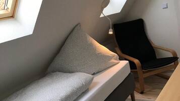 Una habitación estilo loft con techo inclinado, un sofá, una silla y una mesa.