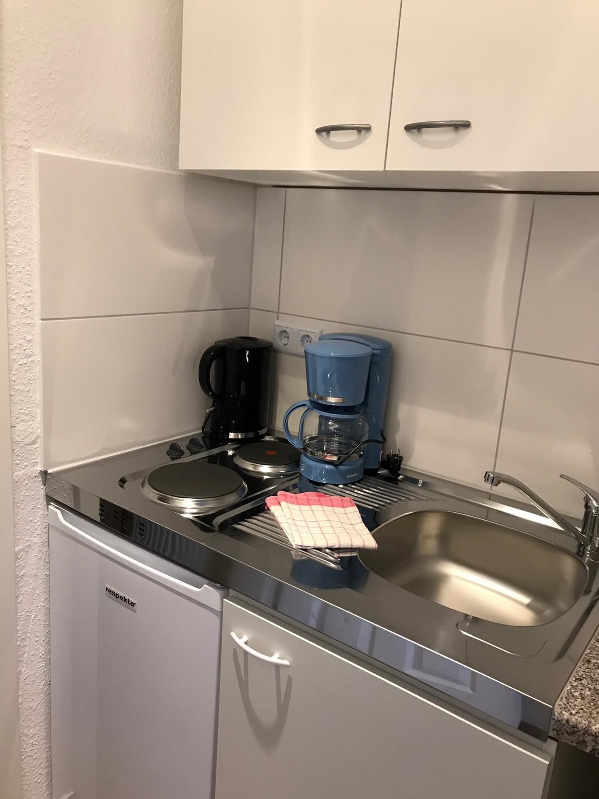 A compact kitchen with a stainless steel sink, a black coffee maker, and a blue coffee maker on the countertop.