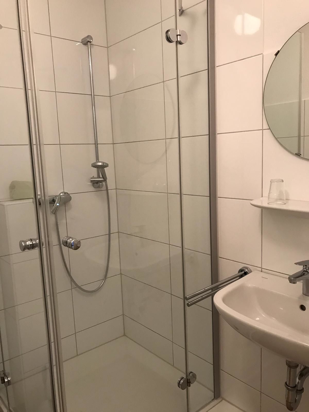 Une salle de bain moderne avec une douche à parois de verre, un lavabo blanc et un miroir rond.