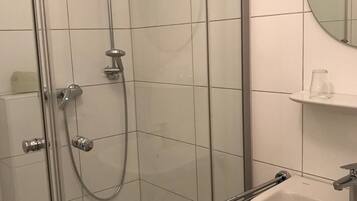 Une salle de bain moderne avec une douche à parois de verre, un lavabo blanc et un miroir rond.