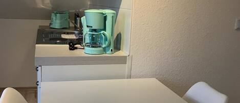 A small kitchenette with a coffee maker, a sink, and a white table with two chairs.