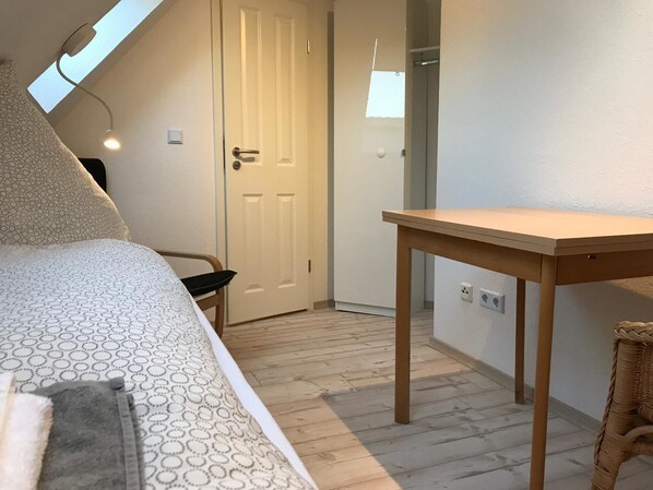 A bedroom with a bed, a wooden table, a chair, a door, and a skylight. - Kleine Möwe (Dornum)