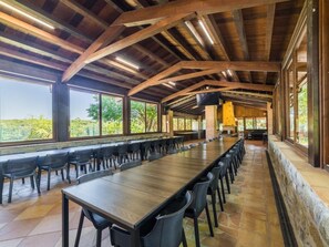 A long dining table with chairs, wooden beams, large windows, and a stone floor. - Villa for 23 people. BBQ, large pool, near Barcelona (Riudarenes)