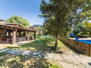 Een overdekt terras met buitenmeubilair, een zwembad met glijbaan en een pad van stenen.