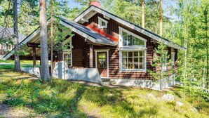 Une cabane en rondins dotée d’un porche couvert et d’une cheminée, entourée d’arbres.