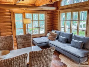 A log cabin interior with a sectional sofa, wicker chairs, and a dining table.