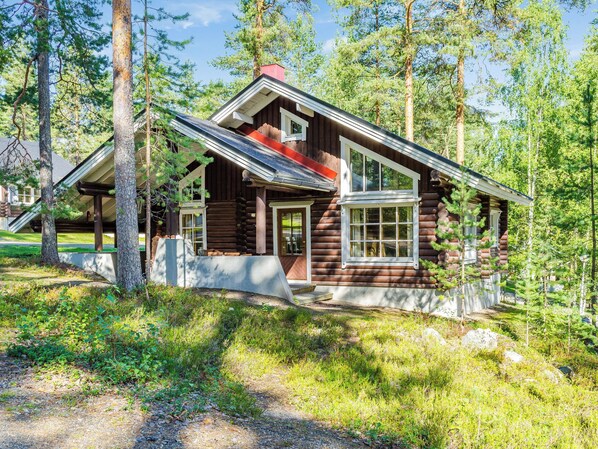 A log cabin with a porch, large windows, and a chimney.