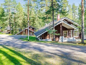 A log cabin with a porch and a chimney, surrounded by a forest.