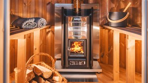 A wooden sauna with a Harvia wood-burning stove, a woven basket of firewood, and a rolled towel on a shelf. - The Hideaway & Spa Terrace at Tregoose Old Mill (Newquay)
