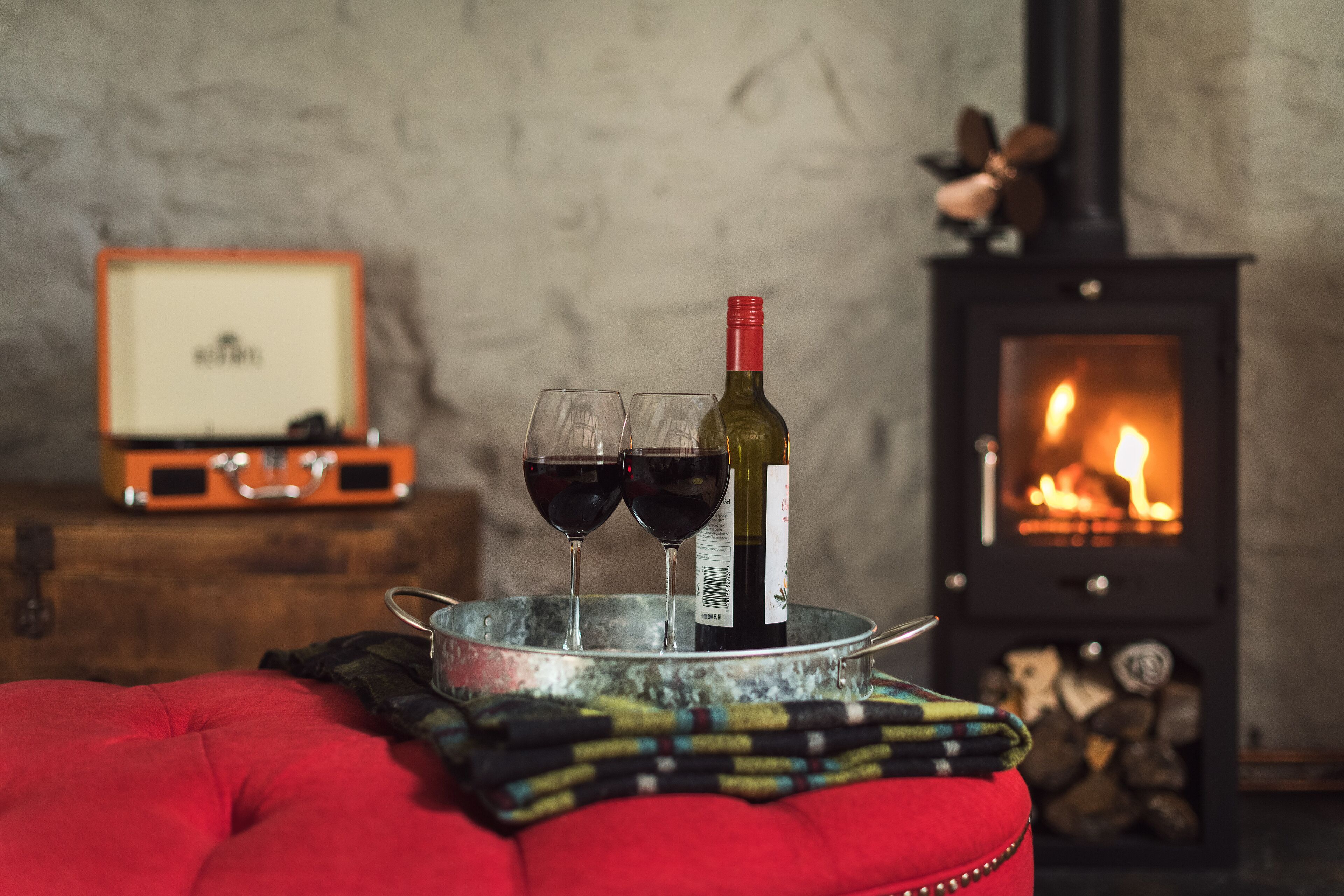 A cozy room with a fireplace, a metal tray with wine glasses and a bottle, and a vintage suitcase.
